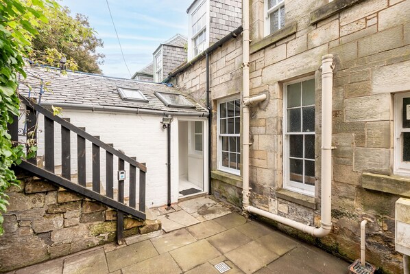 A narrow stone pathway leading to a white building with a black staircase and a small window.