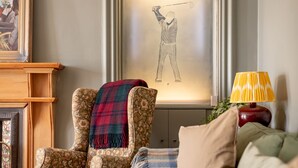 Une pièce comprenant un fauteuil à motifs floraux, une œuvre d’art encadrée représentant un golfeur et une lampe posée sur une table d’appoint.