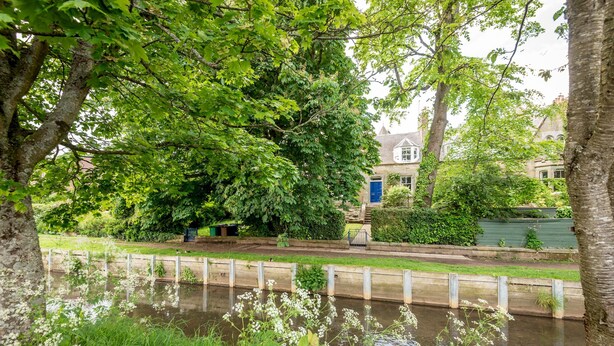 Une vue paisible sur la rivière, avec une promenade en bois, une végétation luxuriante et un bâtiment traditionnel en arrière-plan.