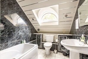 A modern bathroom with a bathtub, toilet, and sink, marble walls, and a skylight. - House on the Burn (St Andrews)