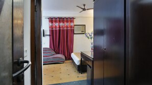 Een kamer met een bed, een bureau, een stoel, een plafondventilator en een raam met gordijnen.