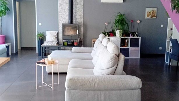 A modern living room with a large sectional sofa, a small side table, a fireplace, and a staircase with a plant on the landing. - Cosy villa in a cul-de-sac, not overlooked. (Gignac)
