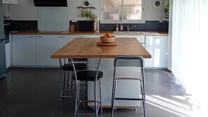 A modern kitchen with a wooden island, two chairs, a hanging light fixture, and a window with curtains. - Cosy villa in a cul-de-sac, not overlooked. (Gignac)