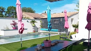 An outdoor patio with a pool, green chairs, and pink umbrellas. - Cosy villa in a cul-de-sac, not overlooked. (Gignac)