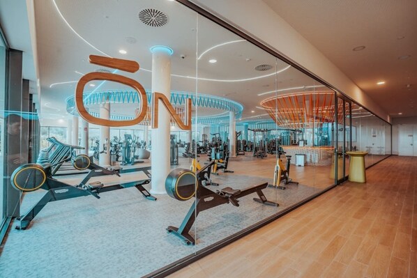 A modern gym with various exercise equipment, a large circular design on the ceiling, and a glass wall.