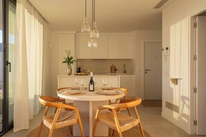 A dining area with a round table, two chairs, a bottle of wine, and a vase of flowers.