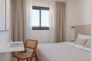 Habitación de hotel con cama, escritorio, silla y ventana con cortinas.
