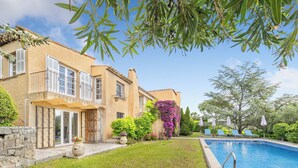 Ein zweigeschossiges Haus mit Swimmingpool, überdachter Terrasse und Garten mit verschiedenen Pflanzen und Blumen.