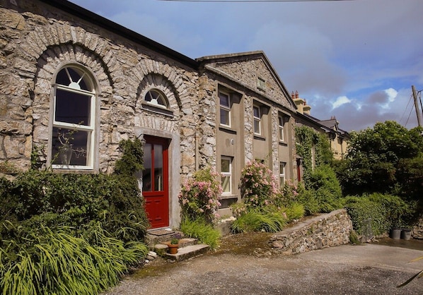 A stone building with a red door, arched windows, and a garden with various plants.
