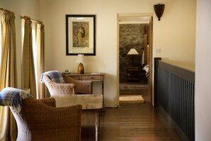 A hallway with a wooden floor, a wicker chair, a table with a lamp, and a framed picture on the wall. - Old School House, Clifden (Clifden)
