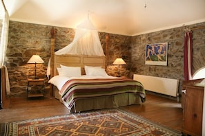 A bedroom with a stone wall, a bed with a canopy, two bedside lamps, and a patterned rug.