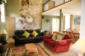 A living room with a stone wall, a black leather sofa, a red sofa, a wooden coffee table, and a dining area with chairs and a table. - Old School House, Clifden (Clifden)