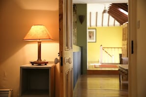 A hallway with a lamp on a stand, a door, and a staircase leading to another room.