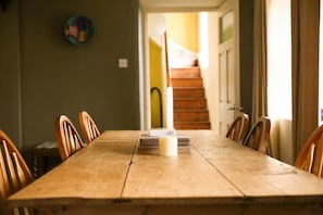 A wooden dining table with chairs, a candle, and a stack of books. - Old School House, Clifden (Clifden)