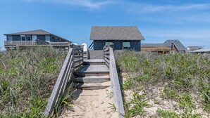A wooden staircase leading to a beach house with a sandy path and beach vegetation. - The Minor Manor - NH MP 11.5, Historic Oceanfront, Dunetop Deck, YR Flex Stays (Nags Head)
