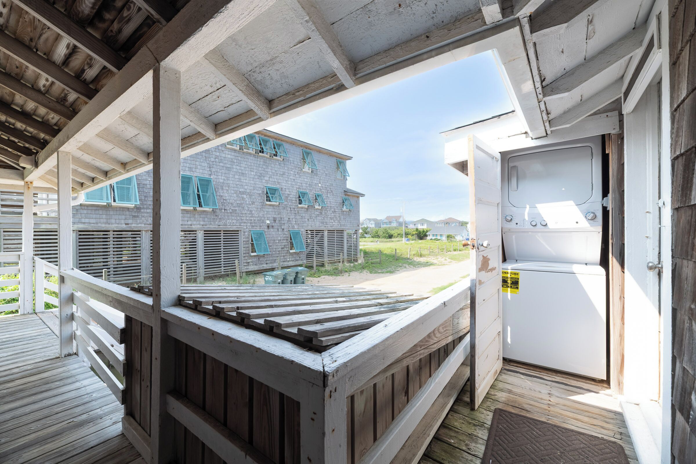 A covered outdoor area with a wooden deck, a view of a building with multiple windows, and a white appliance on the right.