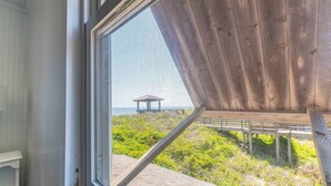 A window with a view of a grassy area and a structure with a roof. - The Minor Manor - NH MP 11.5, Historic Oceanfront, Dunetop Deck, YR Flex Stays (Nags Head)