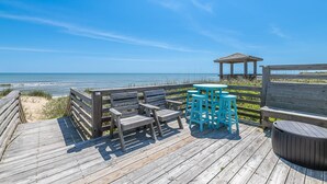 A wooden deck with a gazebo, a table with chairs, and a trash can. - The Minor Manor - NH MP 11.5, Historic Oceanfront, Dunetop Deck, YR Flex Stays (Nags Head)