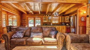 A cozy cabin interior with a leather sofa, a wooden dining table, and a kitchen area with a refrigerator and cabinets. - 3C Ranch on the Road to Yosemite (Groveland)