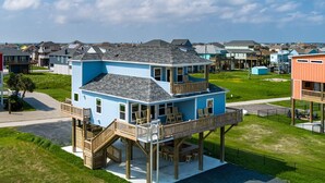 Une maison à deux étages dotée d’un balcon et d’une terrasse, entourée d’une pelouse et d’autres maisons.