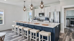 Une cuisine moderne avec des meubles blancs, un îlot central doté de tabourets, des appareils en acier inoxydable et des luminaires décoratifs suspendus.