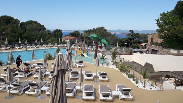 A poolside area with lounge chairs and umbrellas, a water slide, and a view of the sea and mountains. - 2 bedroom mobile home in saint-raphaã "l (Saint-Raphaël)