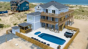 Una proprietà fronte spiaggia con una grande piscina, diverse terrazze e un edificio separato.