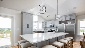 Una cucina moderna con un'isola grande, sgabelli da bar, elettrodomestici in acciaio inossidabile e illuminazione a sospensione.