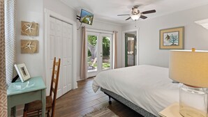A bedroom with a bed, a desk, a chair, a ceiling fan, a TV, and a door leading to an outdoor area. - The Beach is calling you at The Porch Side Cottage, sleeps 9 (St Simons Island)