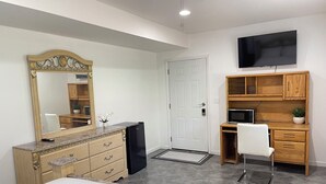Ein Schlafzimmer mit Bett, Kommode, Spiegel, Schreibtisch, Stuhl, Fernseher und einer Tür.