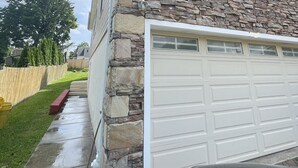 Ein Haus mit Steinaußenwand, einer Garage und einem sichtbaren Wasserschlauch.