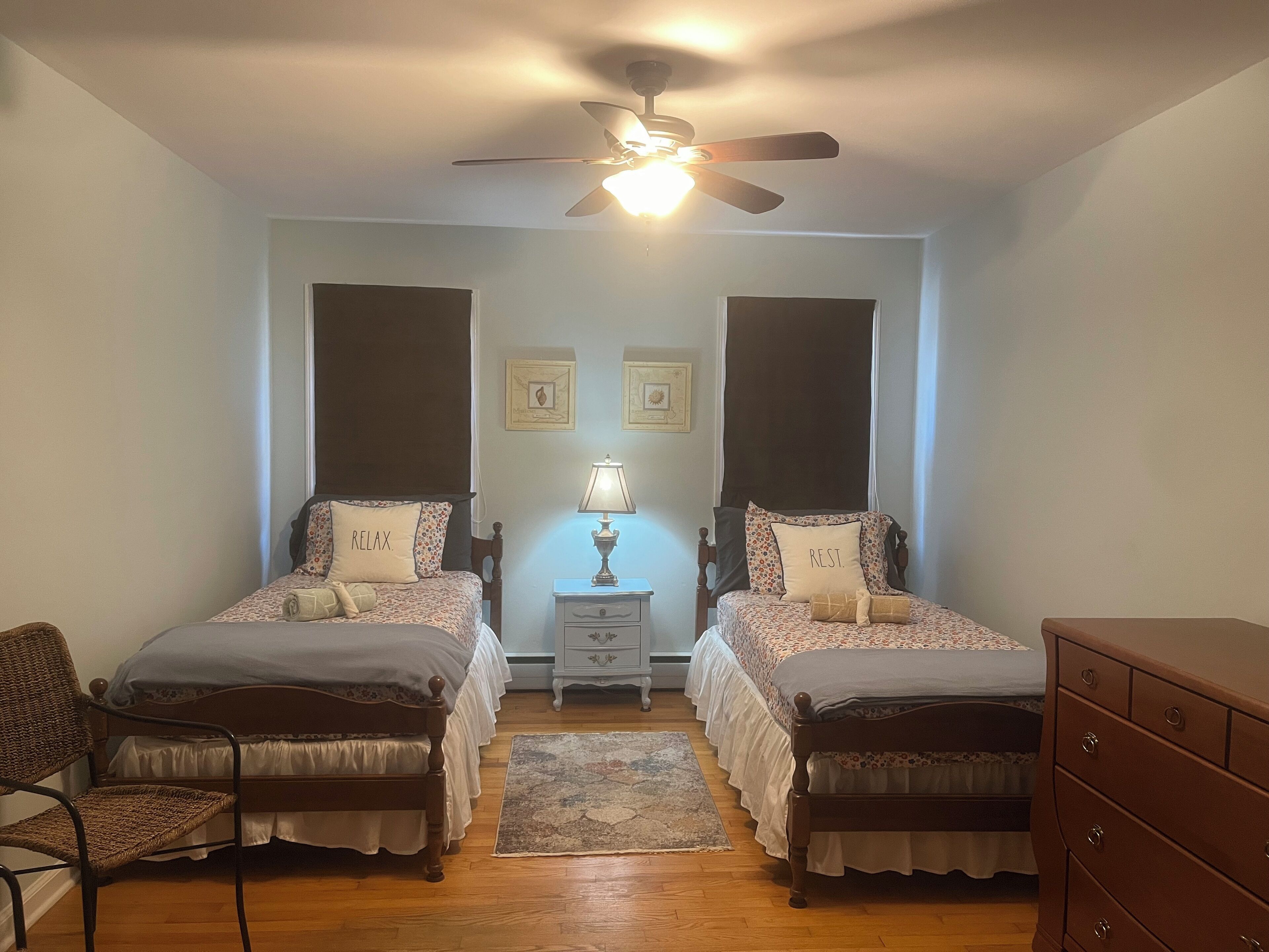 A bedroom with two single beds, a ceiling fan, a nightstand with a lamp, a chair, and a dresser.