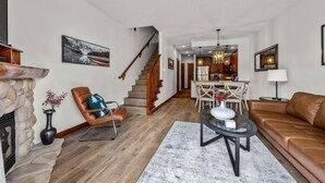 A spacious living room with a stone fireplace, a leather sofa, a dining area with a chandelier, and a kitchen in the background.