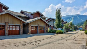 A row of wooden buildings with stone pillars, garage doors, and a clear view of mountains in the background.