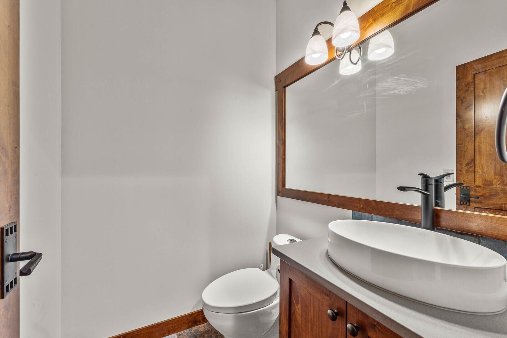 Ein modernes Badezimmer mit Toilette in Weiß, einem großen Waschbecken und einem Spiegel mit Holzrahmen.