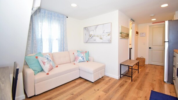 A modern living room with a beige sectional sofa, a small table, and a kitchen area with a refrigerator.