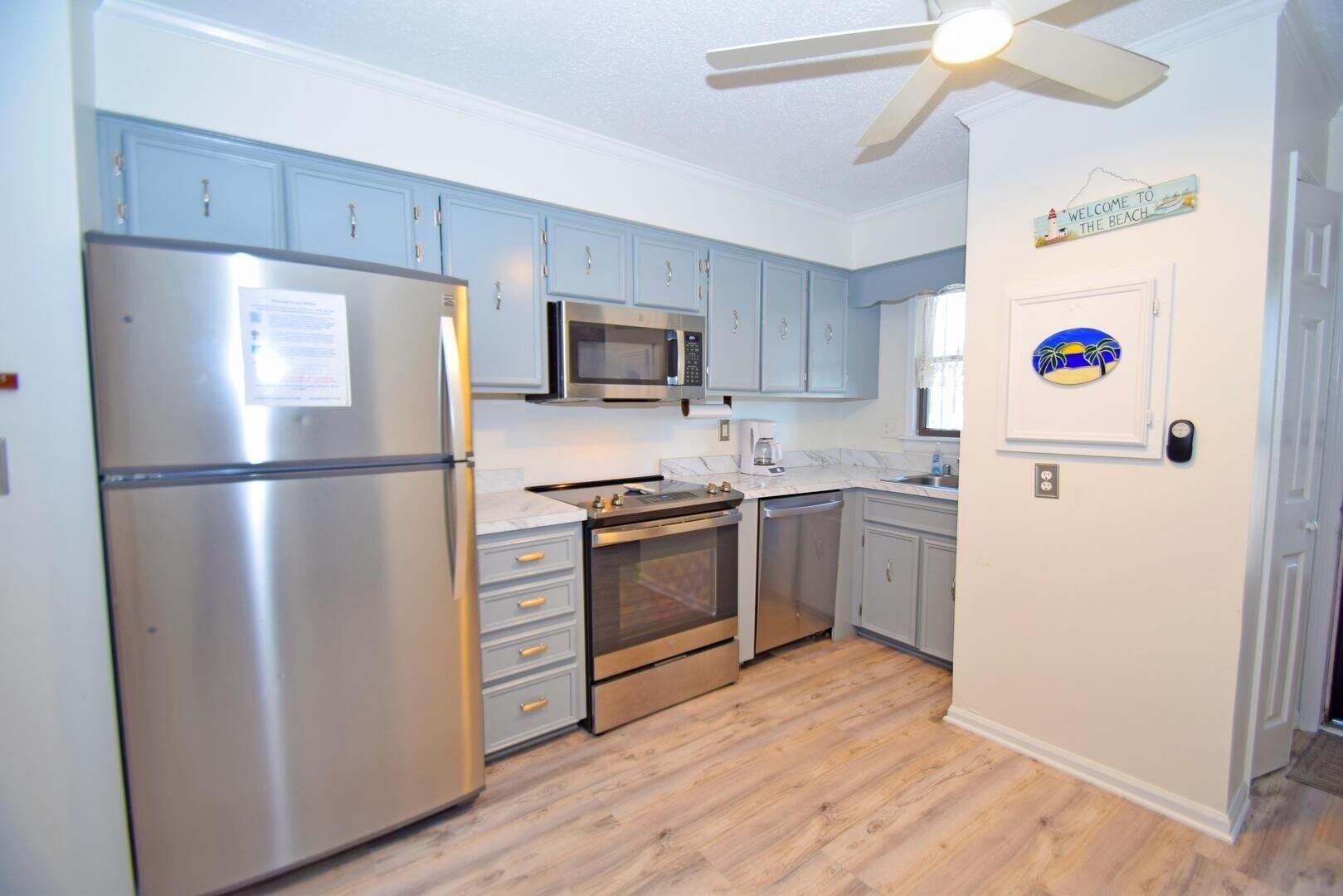 A kitchen with light blue cabinets, stainless steel appliances, and a wooden floor.
