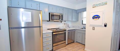 A kitchen with light blue cabinets, stainless steel appliances, and a wooden floor.