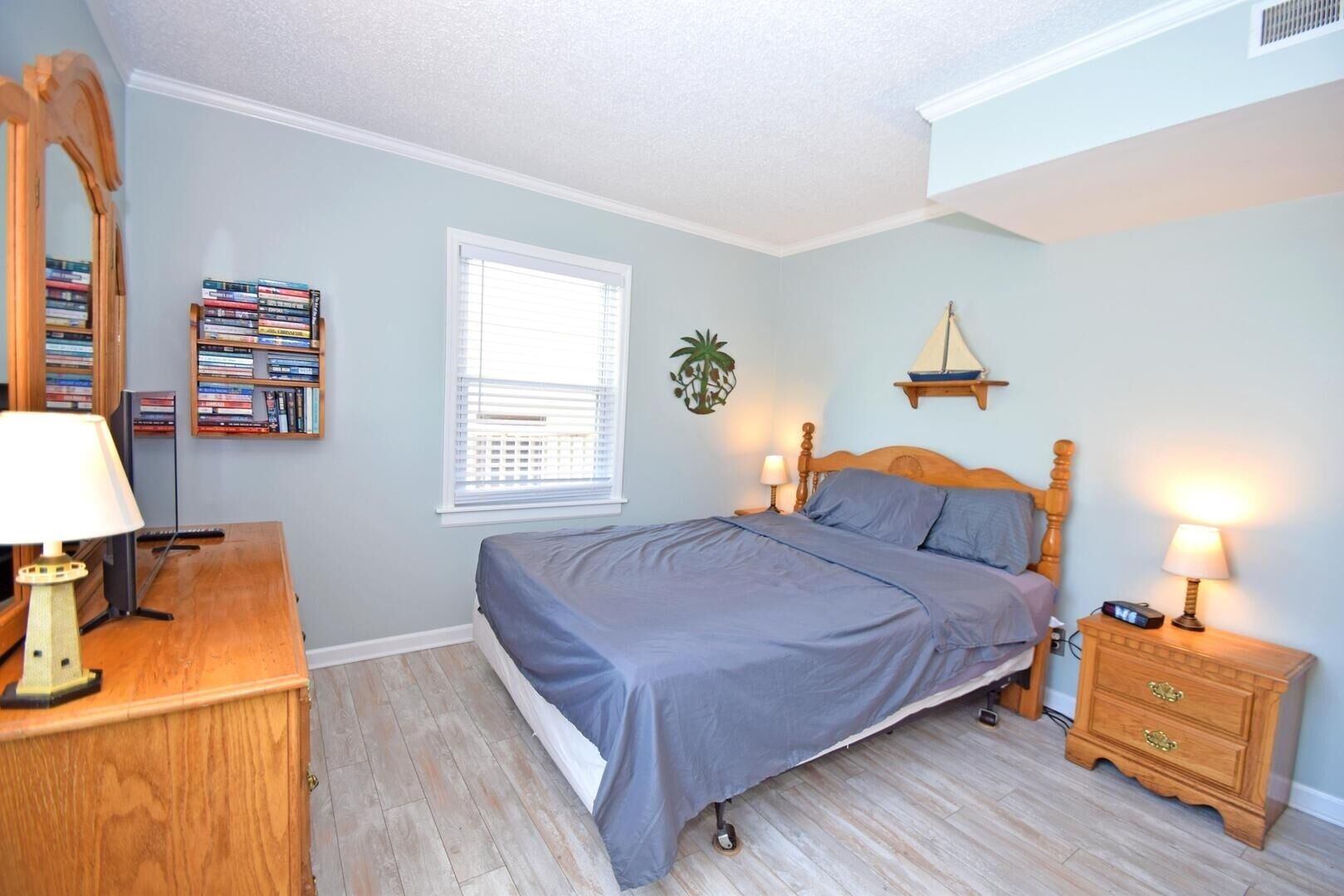 A bedroom with a bed, bedside tables, a dresser, a mirror, a window, and a bookshelf.