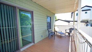 A covered balcony with a sliding glass door, a small table with chairs, and a white railing. - Park Place 101 2 Bedroom Condo by RedAwning (Ocean City)
