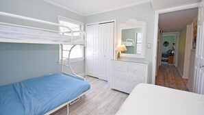 A bedroom with bunk beds, a dresser, a mirror, and a door leading to another room. - Park Place 101 2 Bedroom Condo by RedAwning (Ocean City)