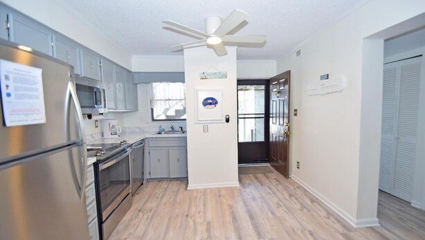 A modern kitchen with stainless steel appliances, a central island, and a ceiling fan. - Park Place 101 2 Bedroom Condo by RedAwning (Ocean City)