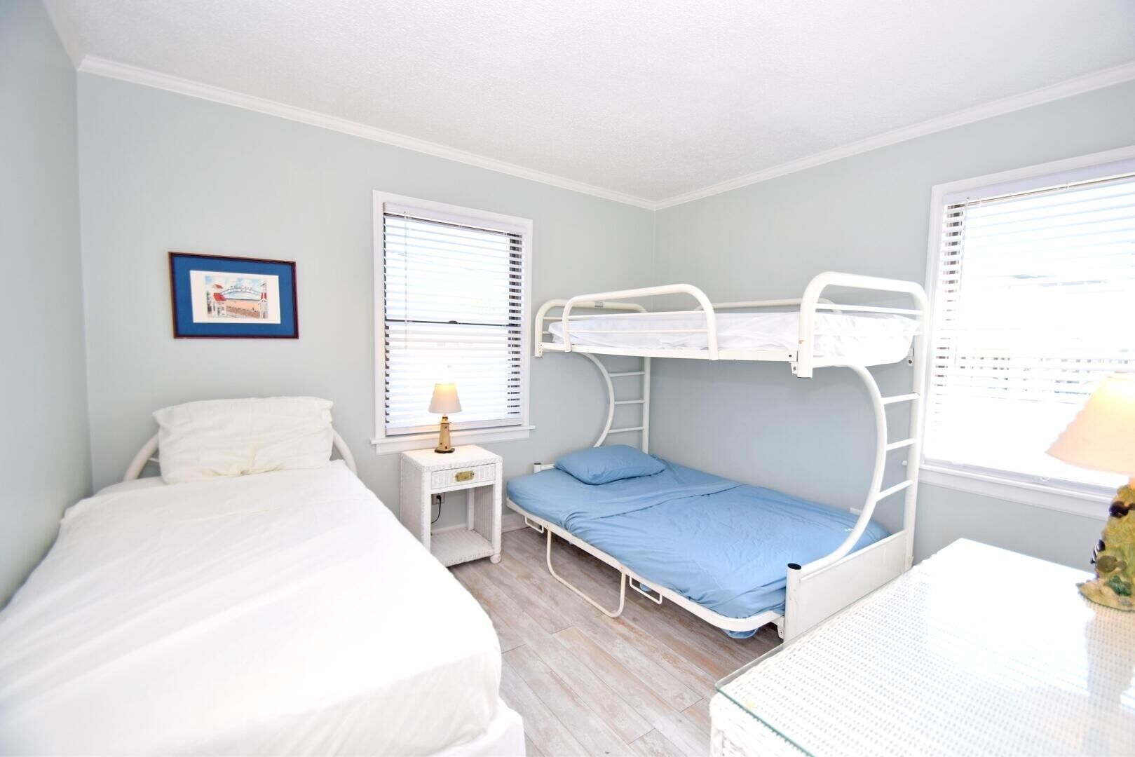A bedroom with bunk beds, a bedside table with a lamp, and a framed picture on the wall.