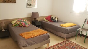 A room with two single beds, a small table with a lamp, a chair, and a patterned rug. - Appartement Climatisé, RDC Villa, Avec Jardin Arboré. Proche Centre Ville Bastia (Ville-di-Pietrabugno)