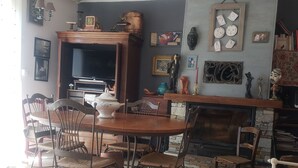 A dining area with a wooden table and chairs, a fireplace, and various wall decorations. - Appartement Climatisé, RDC Villa, Avec Jardin Arboré. Proche Centre Ville Bastia (Ville-di-Pietrabugno)
