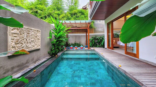 A swimming pool with a wooden deck, surrounded by lush greenery and a decorative wall.