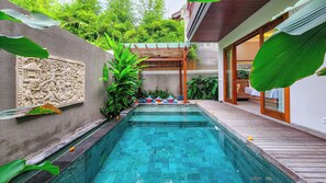 A swimming pool with a wooden deck, surrounded by lush greenery and a decorative wall. - Casa D Gracia Sanur Beach by Nagisa Bali (Denpasar)