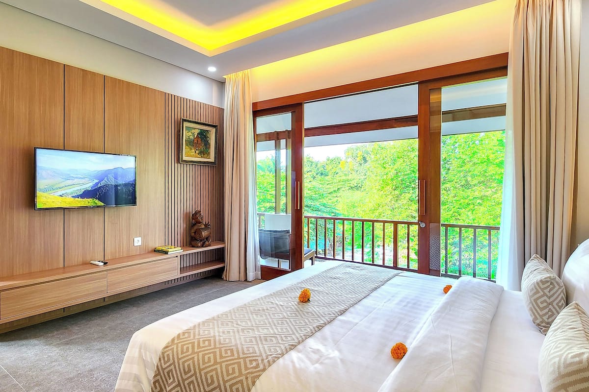 Ein Hotelzimmer mit einem großen Bett, einem an der Wand montierten Fernseher, einem Balkon mit Blick auf Grünflächen und einer Wandverkleidung aus Holz.