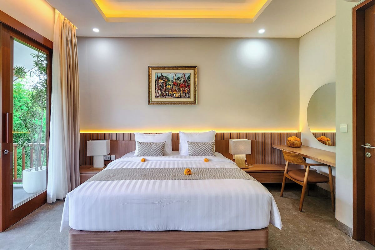 Ein modernes Hotelzimmer mit einem großen Bett, Nachttischlampen, einem Schreibtisch und Blick auf Grünflächen durch das Fenster.