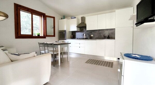 Une cuisine moderne avec des meubles blancs, un coin repas comprenant une table et des chaises, et un four encastré.